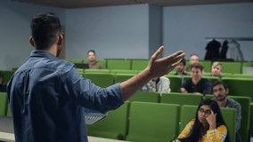 University Professor Explaining the Importance of a College Degree to a Group of Diverse Students in a Modern Auditorium. Teacher Holding a Laptop Computer and Talking to Scholars. Camera Facing Class - Powered by Shutterstock - Get 15% off with code: PIKWIZARD15