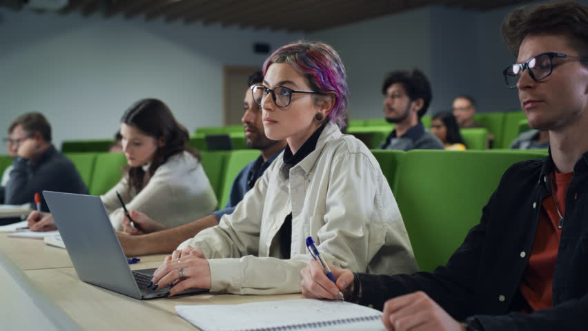 Smart Creative Female Student Studying in University with Diverse Multiethnic Classmates. Young Woman with Colored Short Hair is Using a Laptop Computer. Taking Notes from a Lecture in College Royalty-Free Stock Footage #1103066899