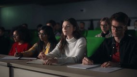 Thoughtful Beautiful Young Female Studying in University, Listening to a Lecture in a Crowded Room with Diverse Multiethnic Classmates. Students Listening to Lecture and Taking Notes in Notebook - Powered by Shutterstock - Get 15% off with code: PIKWIZARD15