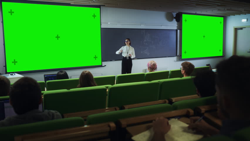 Young University Professor Giving a Lecture, Pointing on a Green Screen Mock Up Display. Group of Smart Diverse Students Study in Modern Classroom. Female Teacher Showing Content on Big Screens