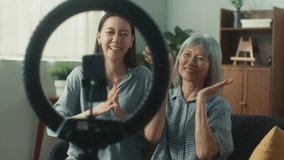 Beautiful Asian woman teaching mother using social media mobile application technology playing and dancing. Happy family daughter and elderly mom sit at living room. Family holiday activity concept