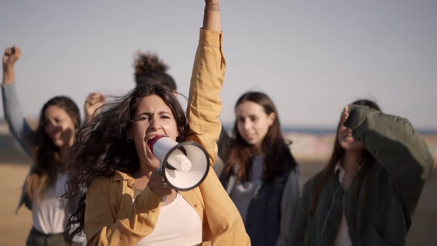 At protest, woman shouts with megaphone raising her fist in crowd. People demonstrating for their rights. High quality FullHD footage Royalty-Free Stock Footage #1103071345