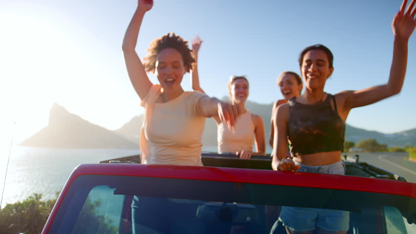 Portrait of female friends standing up through sunroof of car laughing on road trip through countryside with friends - shot in slow motion Royalty-Free Stock Footage #1103072253