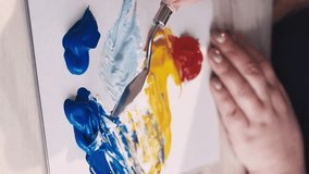 Vertical video. Art studio. Female artist. Creative process. Unrecognizable woman mixing paints colors for creating abstract picture on board canvas with spatula.