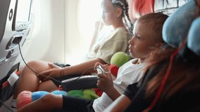 Kid boy playing video game with gamepad in hands looks at screen in airplane during long flight. Teen sister girl sits near looks at window on clouds. Family flight with children on vacation concept. - Powered by Shutterstock - Get 15% off with code: PIKWIZARD15