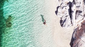 Top view 4K drone video of woman dressed black swimsuit entering a white pebble lonely beach water waves. Exotic tropical summer holidays concept. Cephalonia island, Greece.