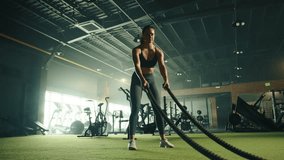Young fit woman doing different exercises on battle rope in well-equipped gym. Treadmills, assault air bikes, cross trainers in the background. High quality 4k footage - Powered by Shutterstock - Get 15% off with code: PIKWIZARD15