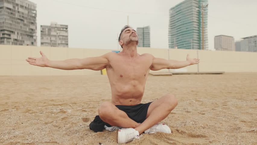 Middle aged athletic man doing relaxing breathing exercises sitting in lotus position on the beach