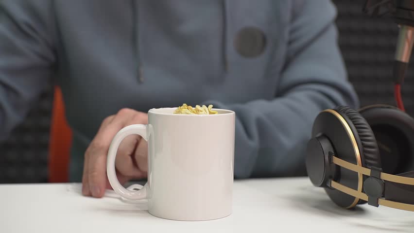 a man in a hoodie eats instant noodles from a mug. real time video. High quality Full HD video recording