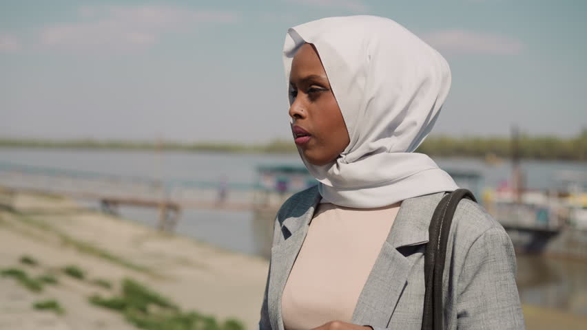 Sorrowing African-American woman with headscarf stands on embankment closeup slow motion. Unhappy Muslim lady at riverside. Heartbroken person portrait | Shutterstock HD Video #1103079647