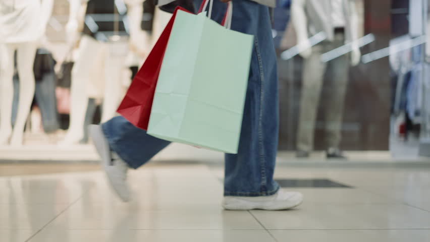 Woman legs in jeans and sneakers walking across mall closeup slow motion. Lady customer holds shopping bags after visiting fashion stores. Hobby and leisure Royalty-Free Stock Footage #1103079691