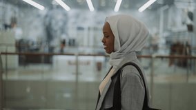 Happy African-American lady with chiffon hijab walks along hall in shopping mall side view slow motion. Muslim woman with handbag does shopping in center - Powered by Shutterstock - Get 15% off with code: PIKWIZARD15