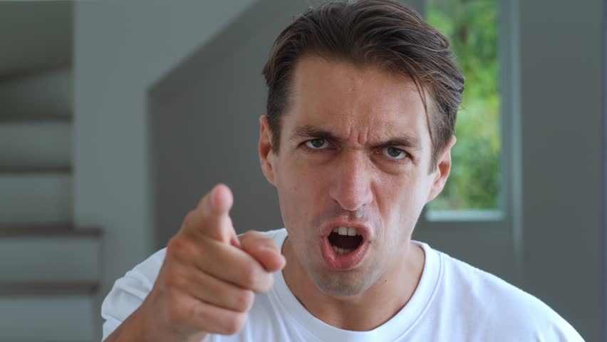 Close-up face of angry man shouting and pointing at camera at home interior. Portrait of aggressive stressed man scolding and shouting. Irritated man threatening with finger and shouting at the camera Royalty-Free Stock Footage #1103085867