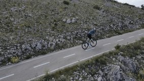 Man on road cycling pushing his bicycle hard in uphill on rural road in Spanish mountains. Camera follows athlete during his intense training in Spanish mountains. Slow motion side video. 