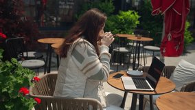 Teenage girl using laptop in cafe outdoor drink coffee. Cheerful young woman sitting watching online student working essay, exam study in flower background