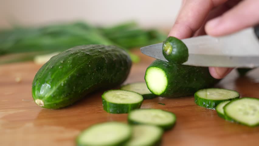 green cucumbers are cut with a knife in the kitchen. healthy food salad vegetables concept. close-up green cucumbers in the kitchen hands close-up cut lifestyle into slices