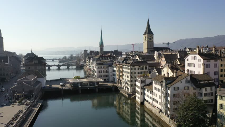 Drone view of Zurich’s old town with Limmat River, traditional houses and church spires under clear sky. Beautiful Swiss cityscape blending history, nature, and urban life.