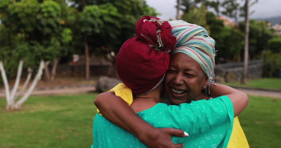 Happy african mother and daughter having tender moment hugging each other at park while wearing traditional afro dress - Family love concept