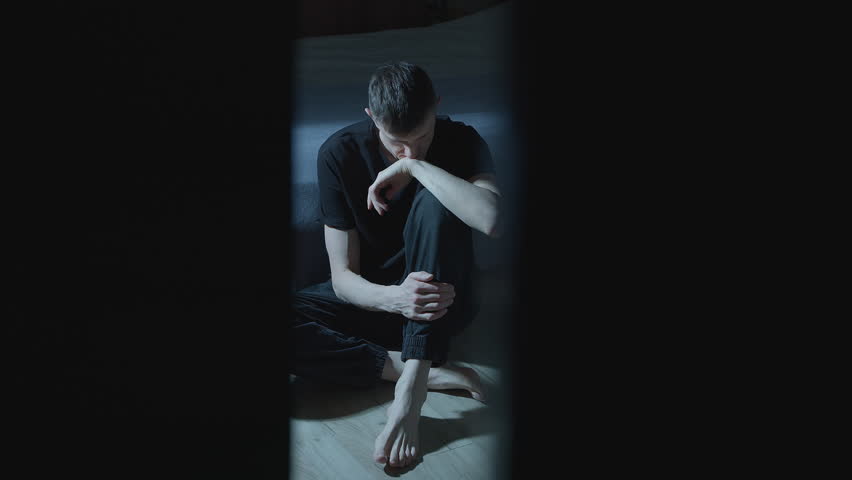Lonely, sad man sits in a dark room. The concept of mental health. Depression.