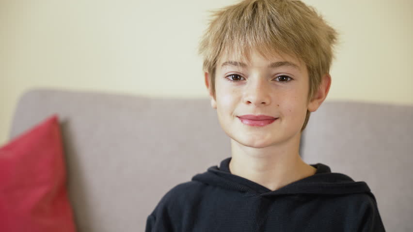 Portrait of handsome boy teenager looking to camera, smiling, making heart shape with hands. Happy child at home interior