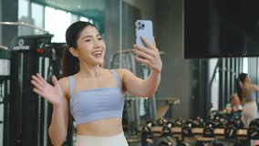 Young asian athletic woman with perfect body wearing sportswear making video call with smart phone to friends or family to show her achievements and results while workout in gym, slow motion