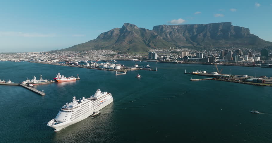 Aerial zoom out. Tugs escorting a Cruise ship out Cape Town harbour, Spectacular Table Mountain in the background.travel , tourism , holiday, vacation 
