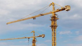 Tower cranes time-lapse on the construction site, against dramatic sky with fast moving clouds. Tall yellow metal structures used for lifting and moving. - Powered by Shutterstock - Get 15% off with code: PIKWIZARD15