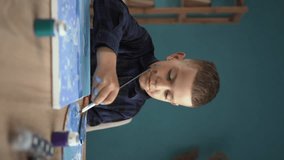 Online education of children. A schoolboy guy watches a video lesson on drawing in a chat, a creative drawing course using a bast shoe at home. vertical video.
