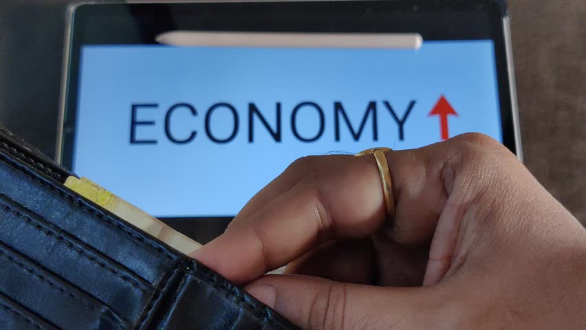 Footage of a person taking out money from his wallet. ECONOMY with an upward pointing arrow is written in background. Footage is depicting economic growth. Royalty-Free Stock Footage #1103118687