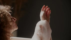 Beautiful woman takes a bubble bath at home. A curly woman applies foam to her hands while taking a bath. - Powered by Shutterstock - Get 15% off with code: PIKWIZARD15