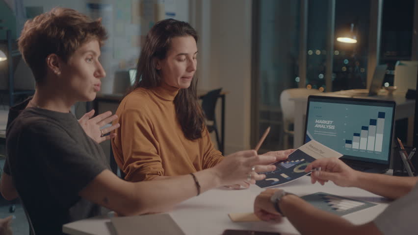 Business team having discussion during night meeting in the office, using laptop and paper slides. Medium shot, overworking concept