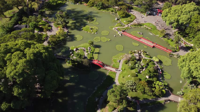 Drone flight over Jardin Japones, Japanese Garden Park in Buenos Aires - People crossing bridge above lake and enjoying beautiful nature at sunny day