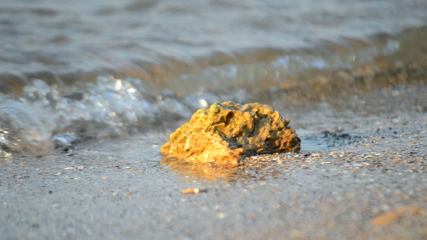 Stone on a sandy beach near the water of the sea waves on the seashore on a sunny summer day. Concept vacation tourism relaxation travel holiday. Nature tropic coast shoreline. Natural background