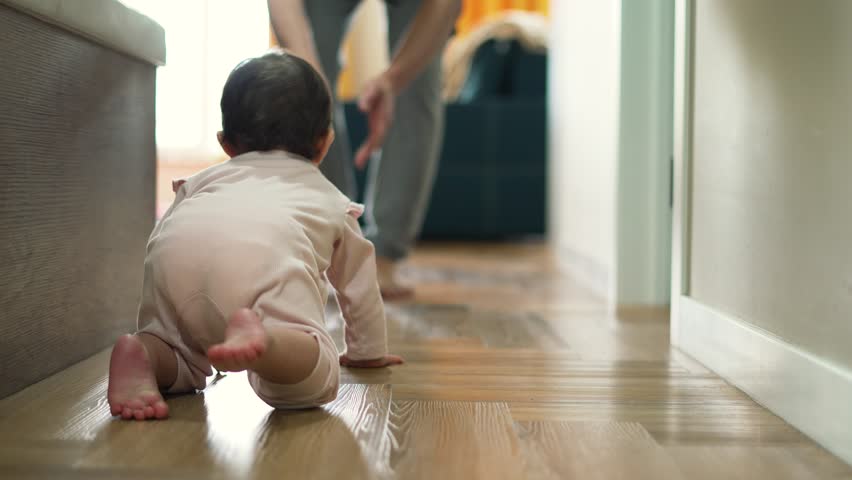 Happy and curious child explores his house by crawling on parquet floor.Father cheers his child up by clapping his hands.Baby crawls across floor towards his parent.Baby learn to move on floor at home Royalty-Free Stock Footage #1103134477