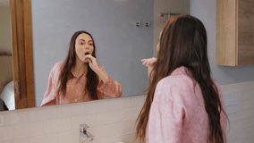 Young caucasian woman in pijamas dances in front of a mirror in a bright bathroom brushing her teeth. Good mood, morning routine. Back view, Video 4k horizontal.