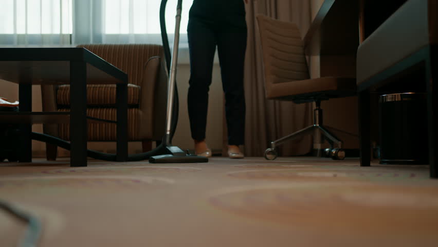 A diligent maid in uniform carefully vacuums the carpet while cleaning the concept of hospitality hotel room
