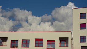 Puffy fluffy white clouds over buildings on blue sky background, summer weather, video loop