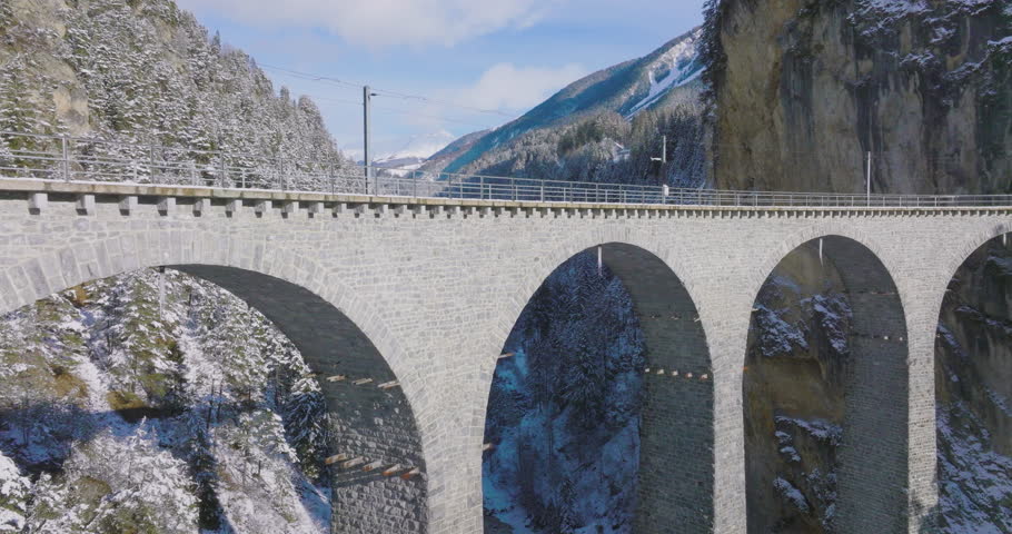 Landwasser Viaduct world heritage sight with luxury Glacier and Bernina express in Swiss Alps snow winter scenery. Aerial Drone shot red train passing through famous mountain in Filisur, Switzerland.