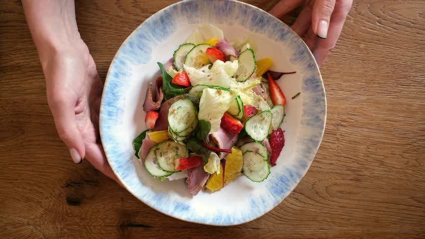 Human hands move plate with delicious and appetizing dish. Healthy balanced salad with meat, vegetables and fruits