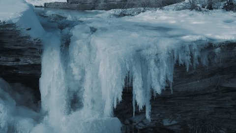Water stream flowing through icicles and rocks in winter. Slow motion. Video de stock