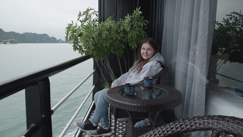 Woman Sitting On The Balcony Of A Cruise Ship. Smiling At Camera While sailing On The Waters Of Halong Bay In Vietnam. wide