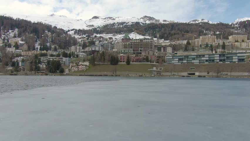 A drone flyover of St Moritz, Switzerland starting from the lake, with snowy mountains in the background