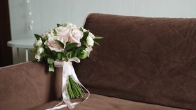Brides bouquet of pink roses with satin ribbon stands on brown upholstered sofa, leaning on armrest. Cozy room with light wall and table. - Powered by Shutterstock - Get 15% off with code: PIKWIZARD15