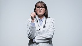 Middle aged confident female doctor talking looking at camera on gray background