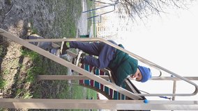 Vertical video - a cautious child descends the stairs on the playground. Development of motor skills and coordination. Copy space - concept of safety rules, physical activity, independence