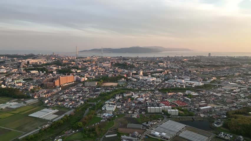 Aerial view of sprawling coastal city with suspension bridge to island at sunset