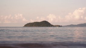 A video of oncoming waves and a view of an island in a distance during daytime in Thailand