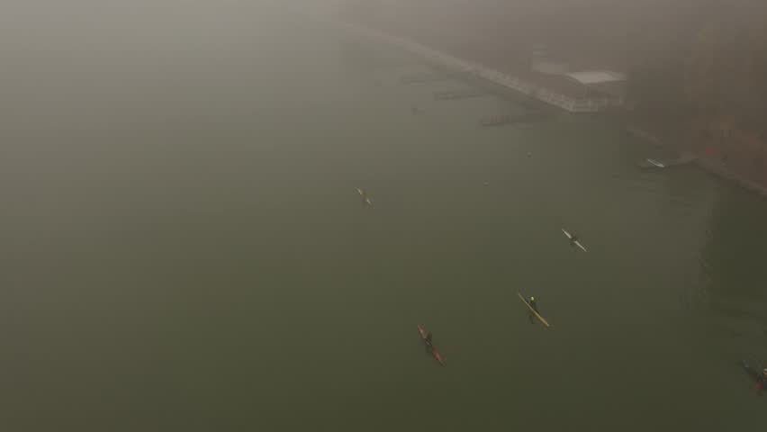 Young people women and men in sportswear on kayaks boats swim paddling along dark gloomy river early morning in autumn spring fog near shore and wooden pier synchronously. aerial top view with drone | Shutterstock HD Video #1103157303