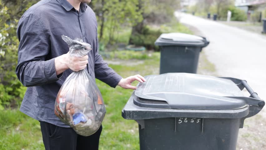 Man throwing out black eco-friendly recyclable trash bag in to big plastic green garbage container. Take out the trash Royalty-Free Stock Footage #1103159203