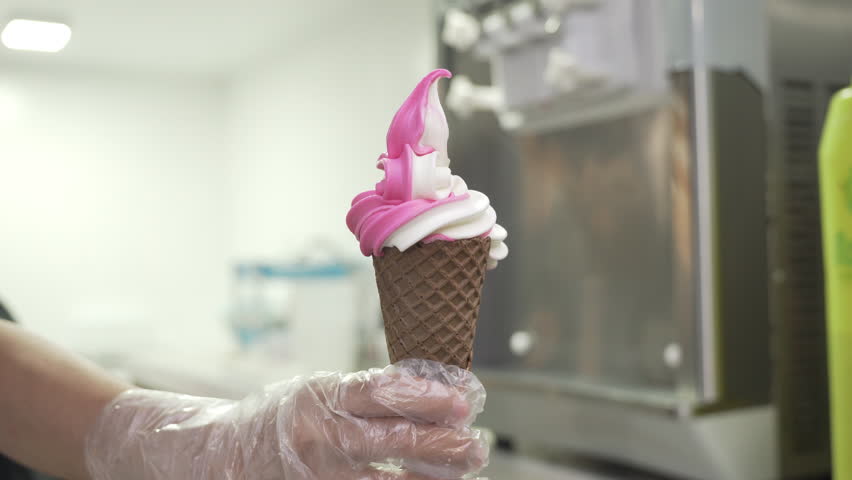 Hand In Disposable Glove Holding Strawberry Vanilla Soft Serve In Ice Cream Cone. closeup